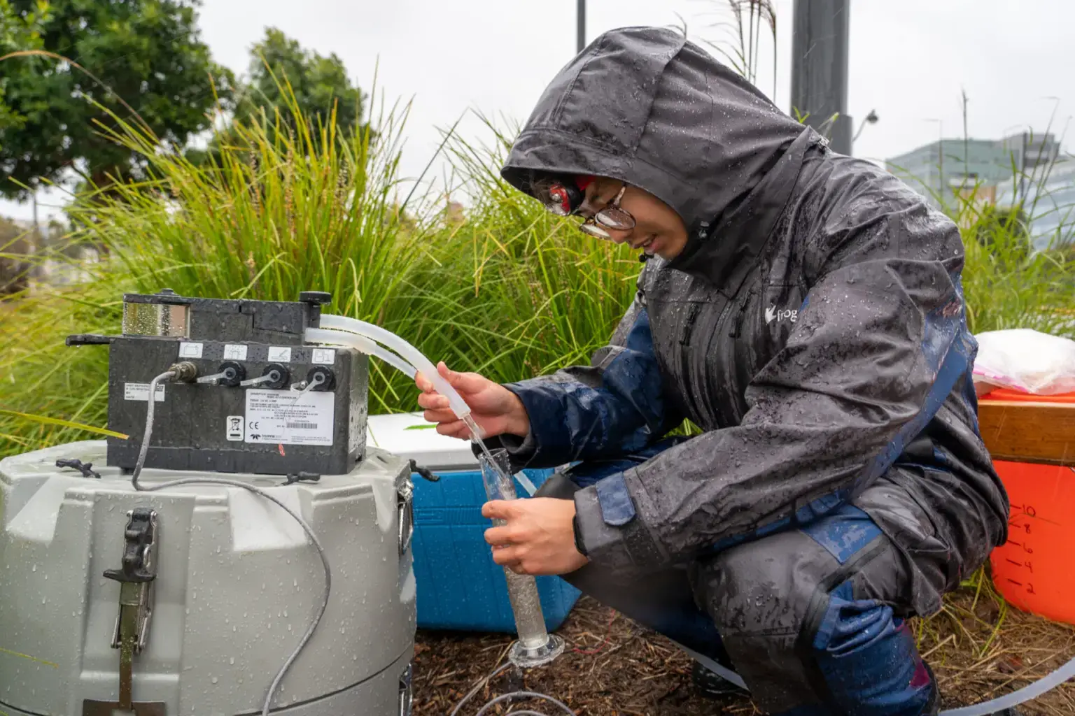A researcher kneels beside a rain garden with a sampling pump collecting stormwater during a December 2022 storm